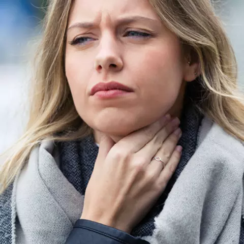 Frau hält sich eine Hand an den Hals. Sie hat Magenbrennen und Reflux